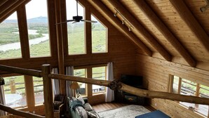 A wooden cabin with a loft bedroom, a dining area, and a living room with a view of a river and mountains. - Yellowstone River Frontage! Beautiful log home on the river with 360  views! (Powell)
