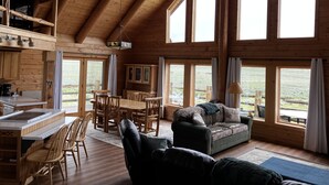 A spacious cabin with a high ceiling, large windows, a dining area, and a cozy living space. - Yellowstone River Frontage! Beautiful log home on the river with 360  views! (Powell)