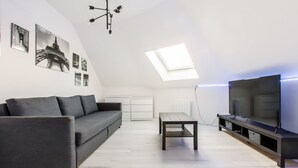 En moderne stue med en grå sofa, et sofabord og et fjernsyn på et stativ.