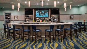 A bar area with a large screen, multiple bar stools, and a bar counter.