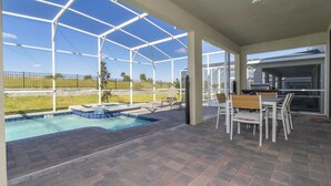 A covered outdoor area with a swimming pool, patio furniture, and a barbecue grill.