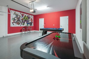 Une salle de billard avec une table de billard, une fresque représentant des personnages de bandes dessinées et un mur rouge.