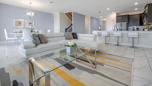 Ein modernes Wohnzimmer mit einem Glastisch, einer Couch und einem Essbereich mit weißen Stühlen.