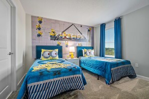 Une chambre avec deux lits, une fresque murale représentant des personnages de dessins animés, et une fenêtre avec des rideaux bleus.