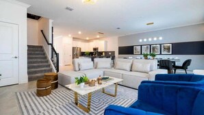 A modern living room with a sofa, coffee table, and blue chairs. There is a staircase leading to another room. - Last Minute Disney! Private Pool, Hot Tub, Game Room & Themed Bedrooms. Book Now! #90505 (Orlando)