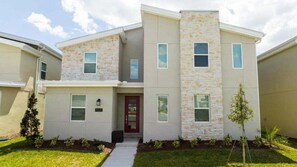 A modern two-story house with a stone facade, a red door, and a small front yard with plants. - Last Minute Disney! Private Pool, Hot Tub, Game Room & Themed Bedrooms. Book Now! #90505 (Orlando)