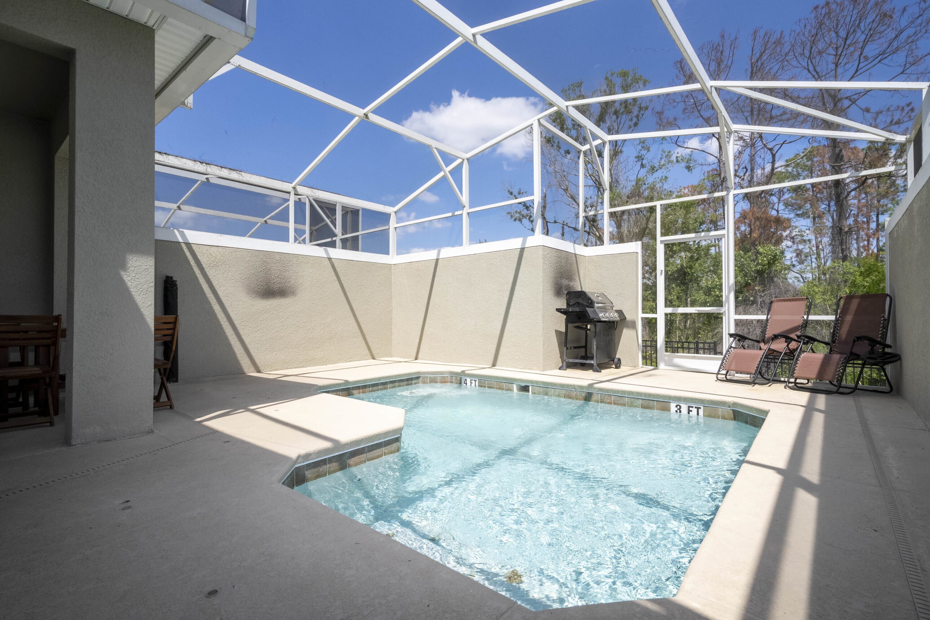 Una piscina con cerramiento de vidrio, rodeada de sillones de descanso y una zona de barbacoa.