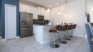 Una cocina moderna con armarios blancos, electrodomésticos de acero inoxidable y una isla central con taburetes de bar.
