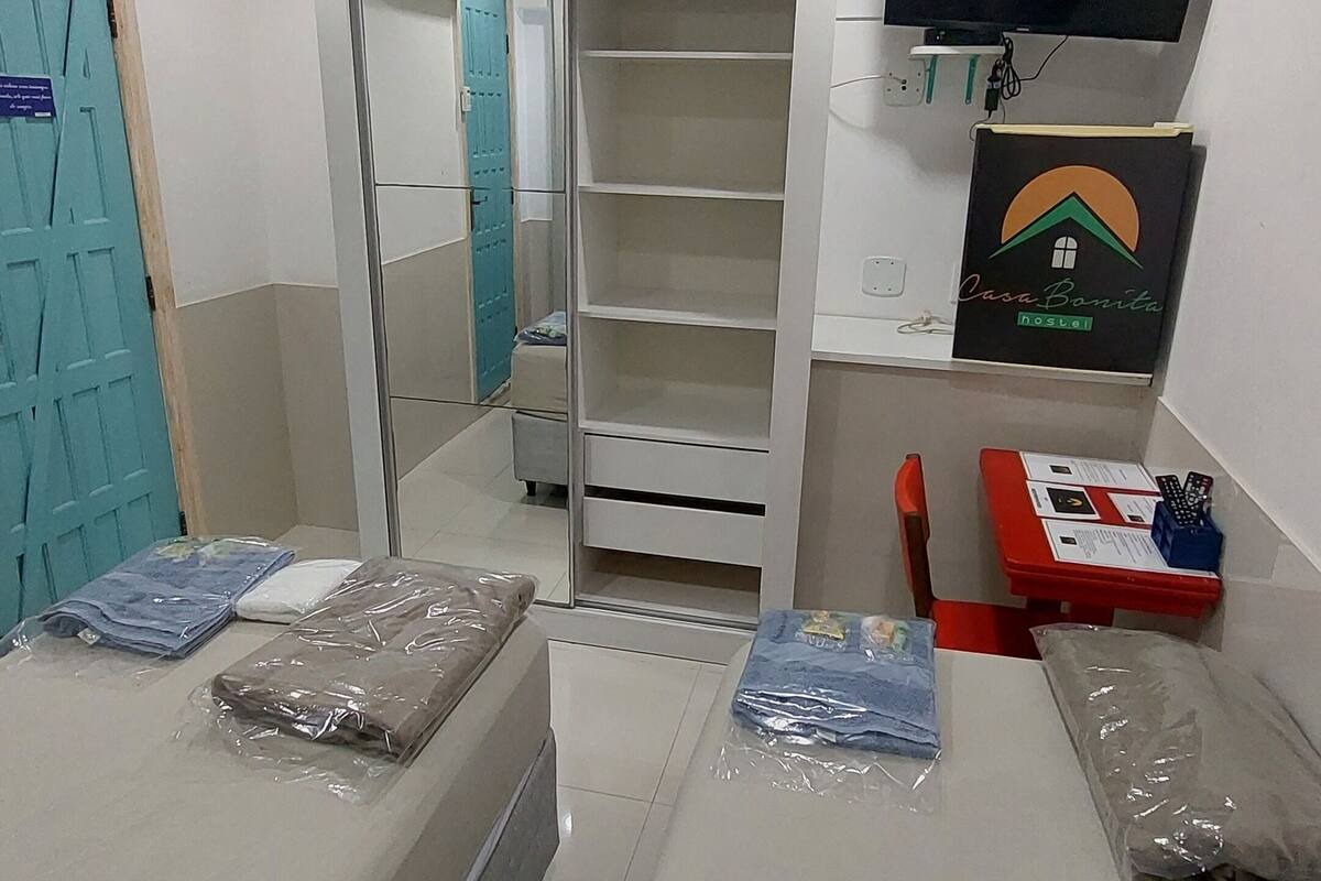 Un dormitorio con cama, armario, escritorio, silla, televisor y ventilador de techo.