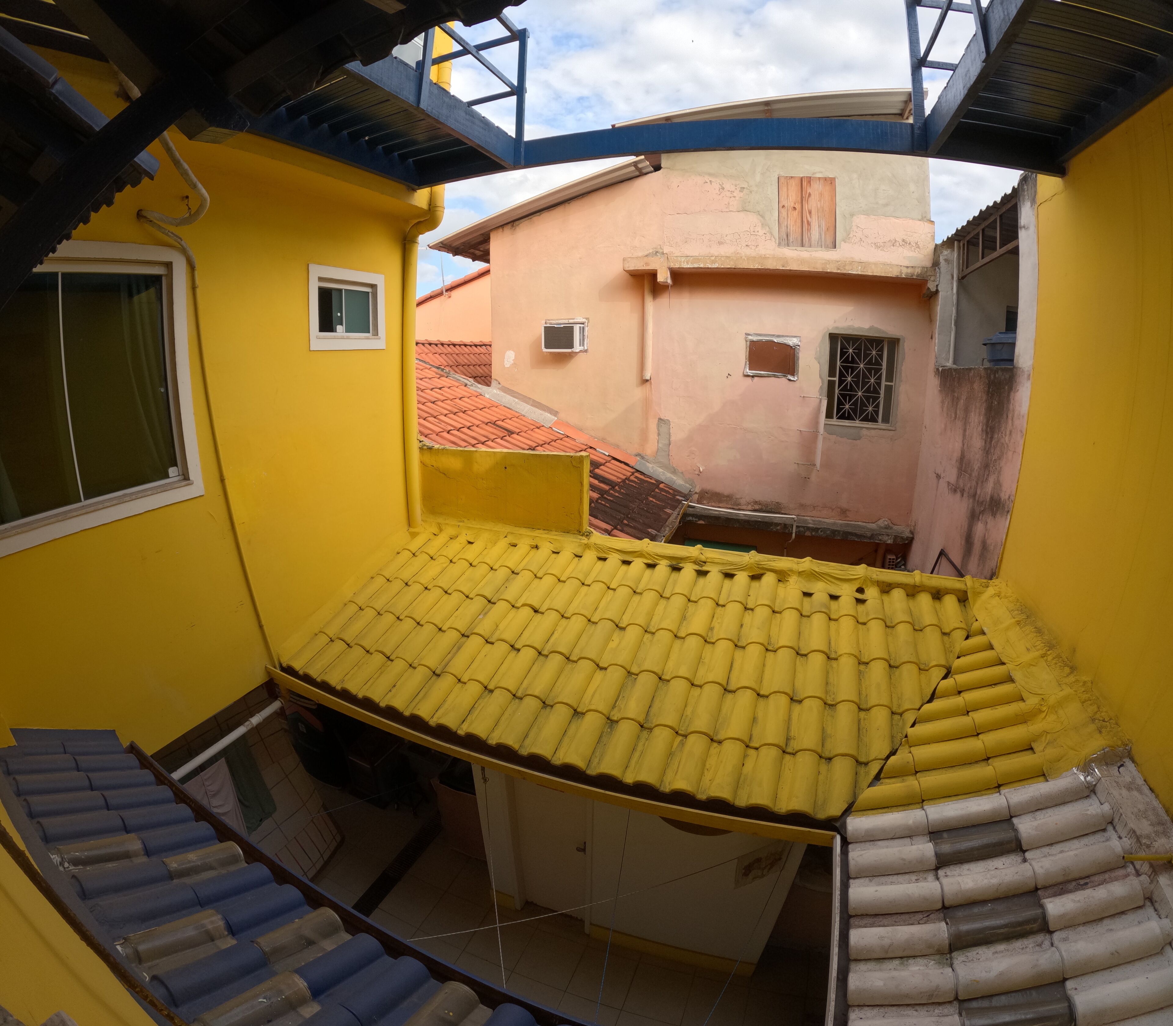 A yellow room with a tiled roof, a window, and a view of neighboring buildings.