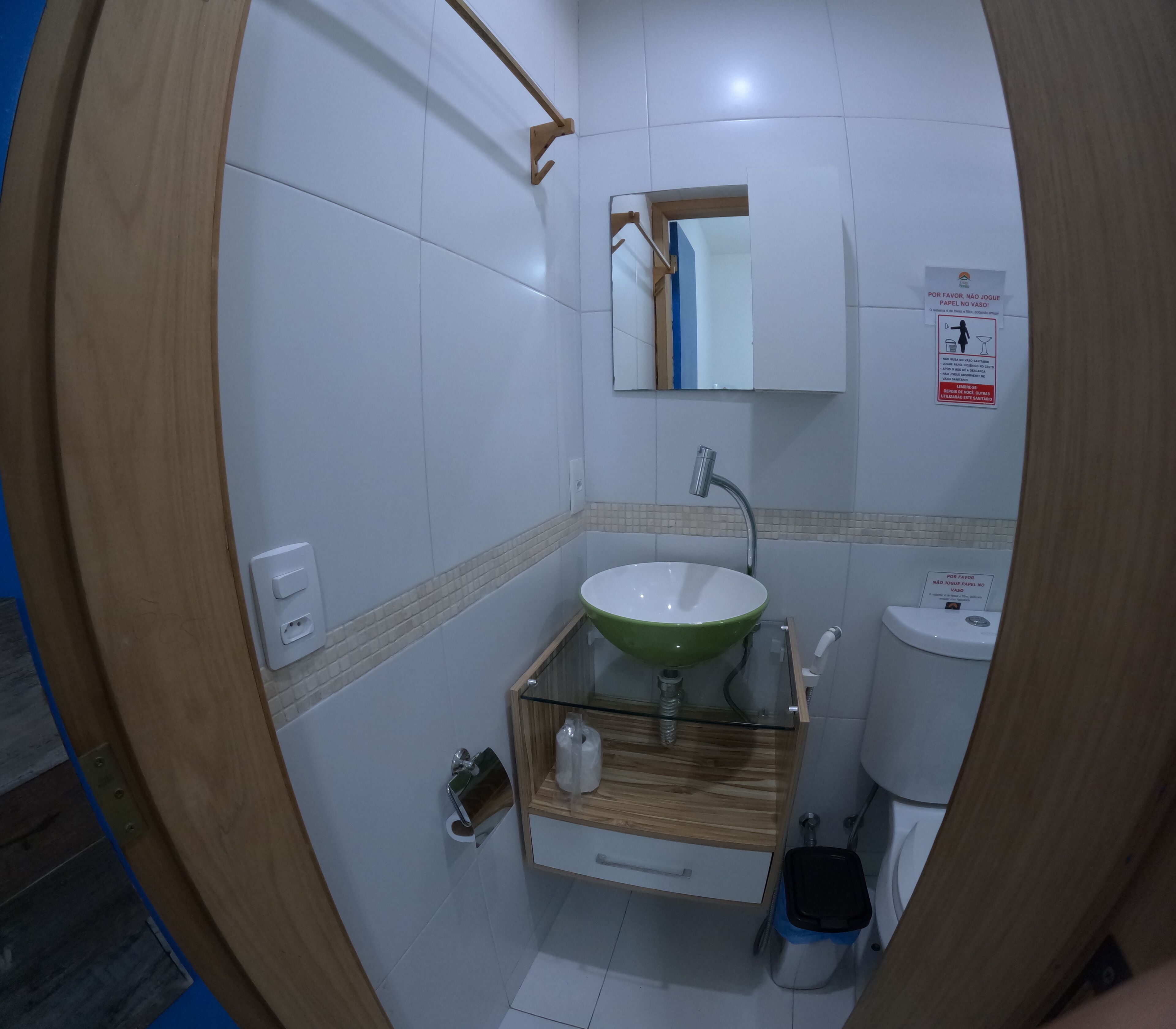 A bathroom with a wooden vanity, a green sink, a mirror, a toilet, and a trash bin.