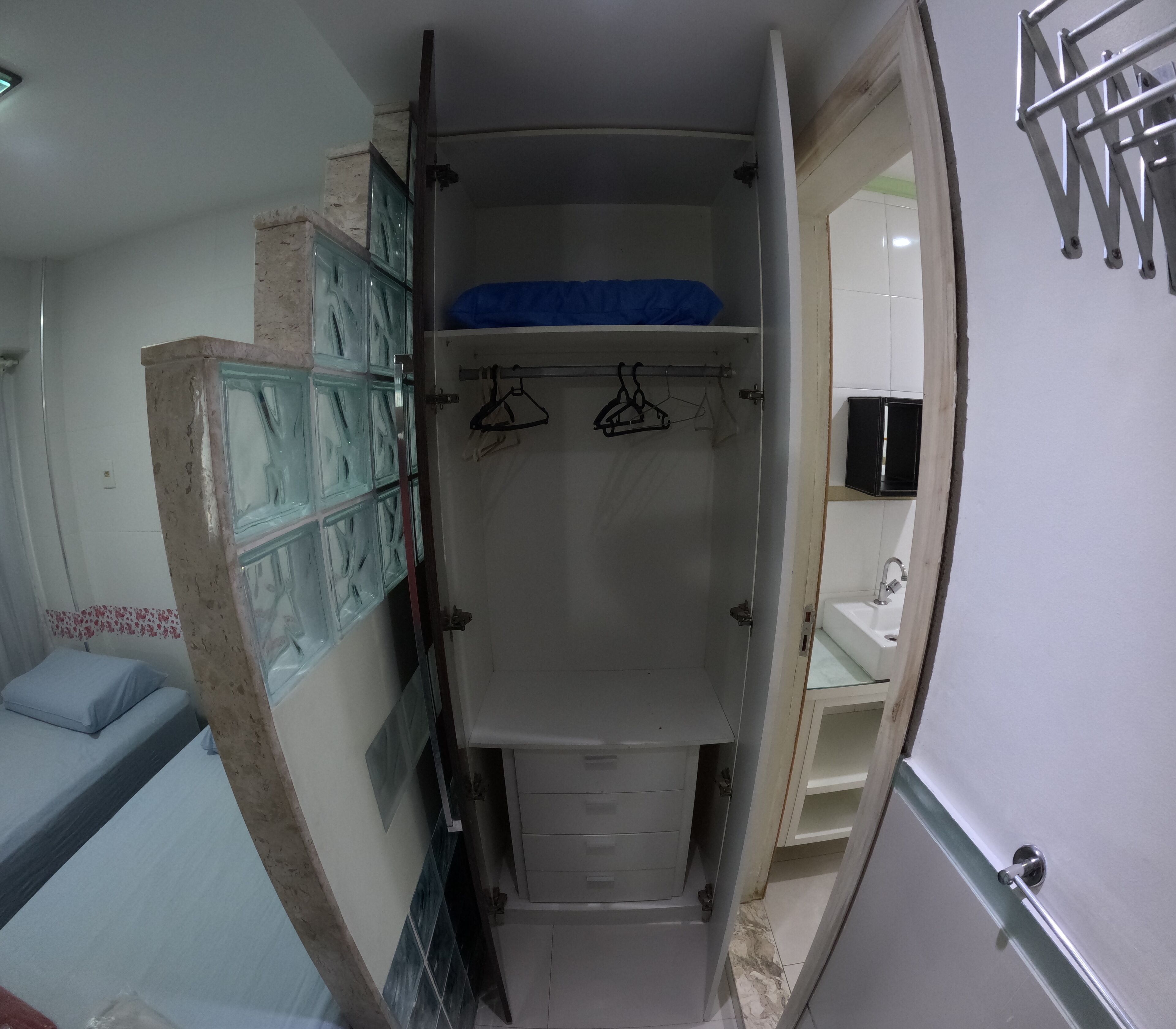 Un pasillo estrecho que conduce a un baño con ducha, una cama con almohada azul y un armario con toalla azul.