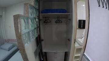 Un pasillo estrecho que conduce a un baño con ducha, una cama con almohada azul y un armario con toalla azul.
