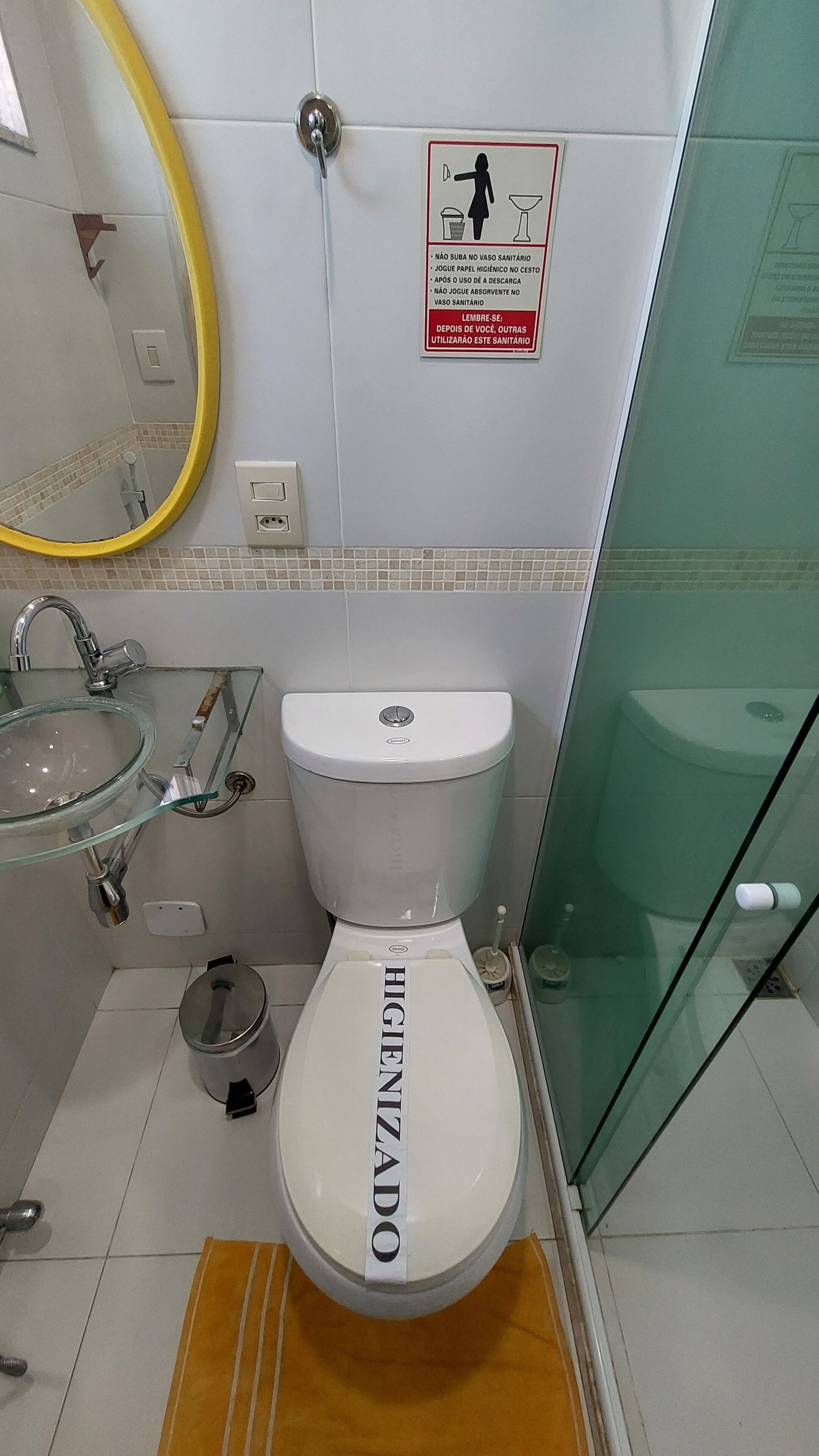 Un baño con inodoro etiquetado como 'HIGIENIZADO', lavabo de cristal, espejo y secamanos.