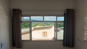 Una habitación con dos camas, un ventilador de techo, una ventana con cortinas y vista a un edificio.