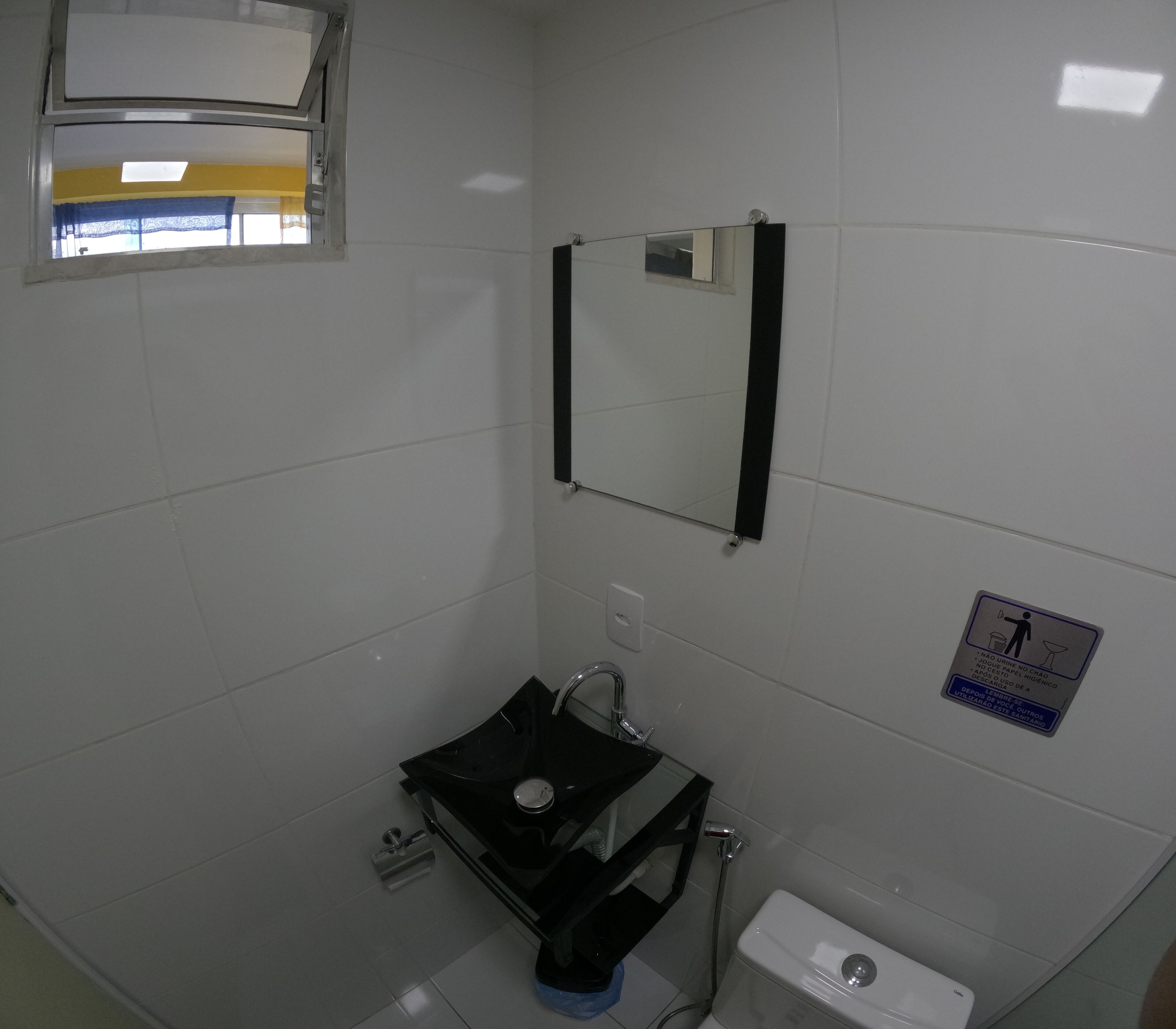 A small bathroom with white tiles, a black sink, a mirror, and a toilet.