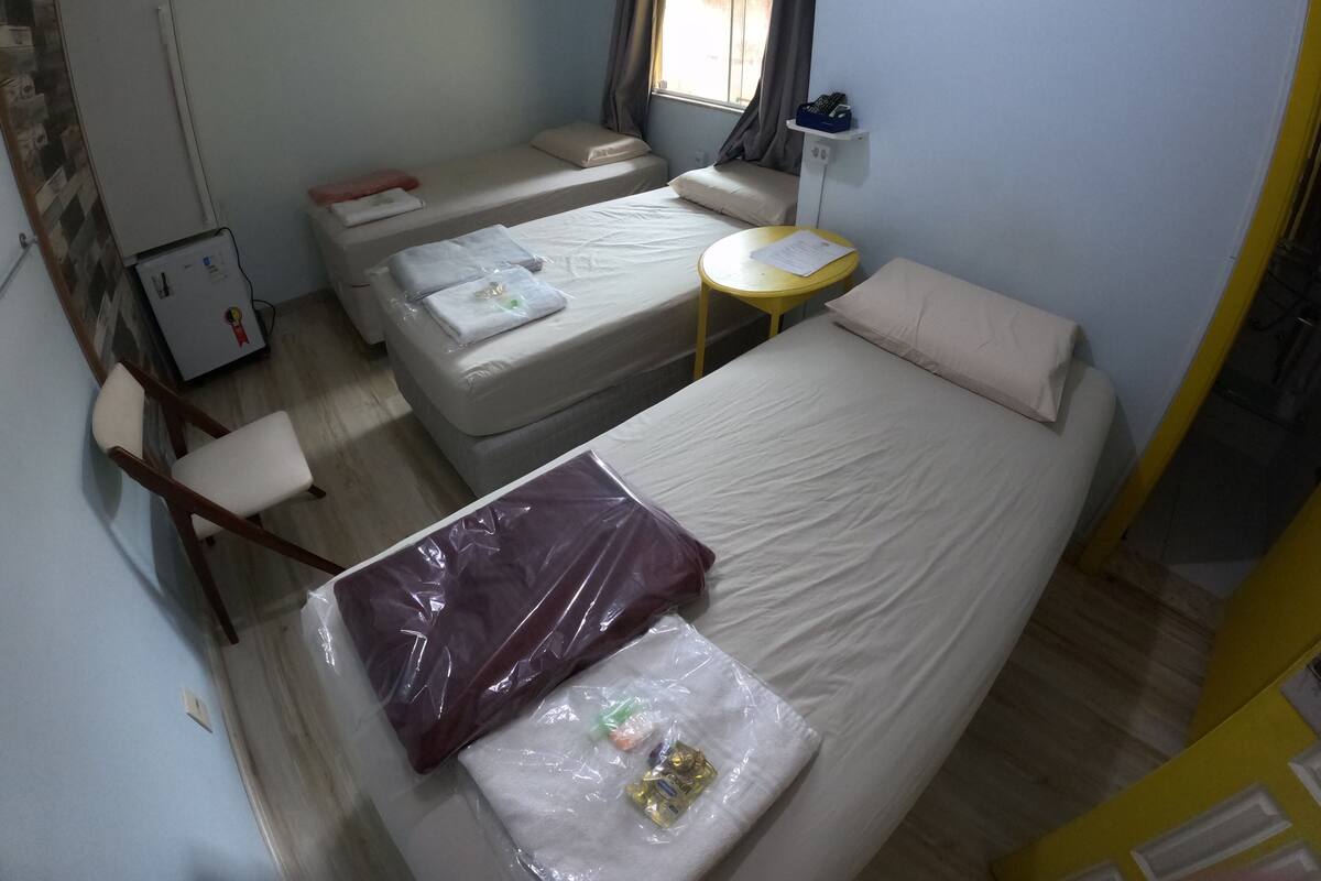 Una habitación compacta con dos camas, una mesita, una silla y una ventana con cortinas.