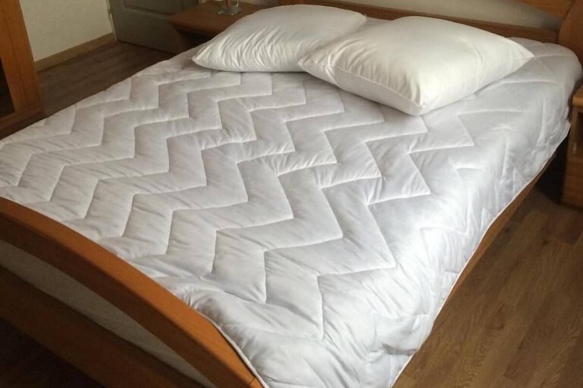 A single bed with a wooden frame, a white quilt, and two pillows.