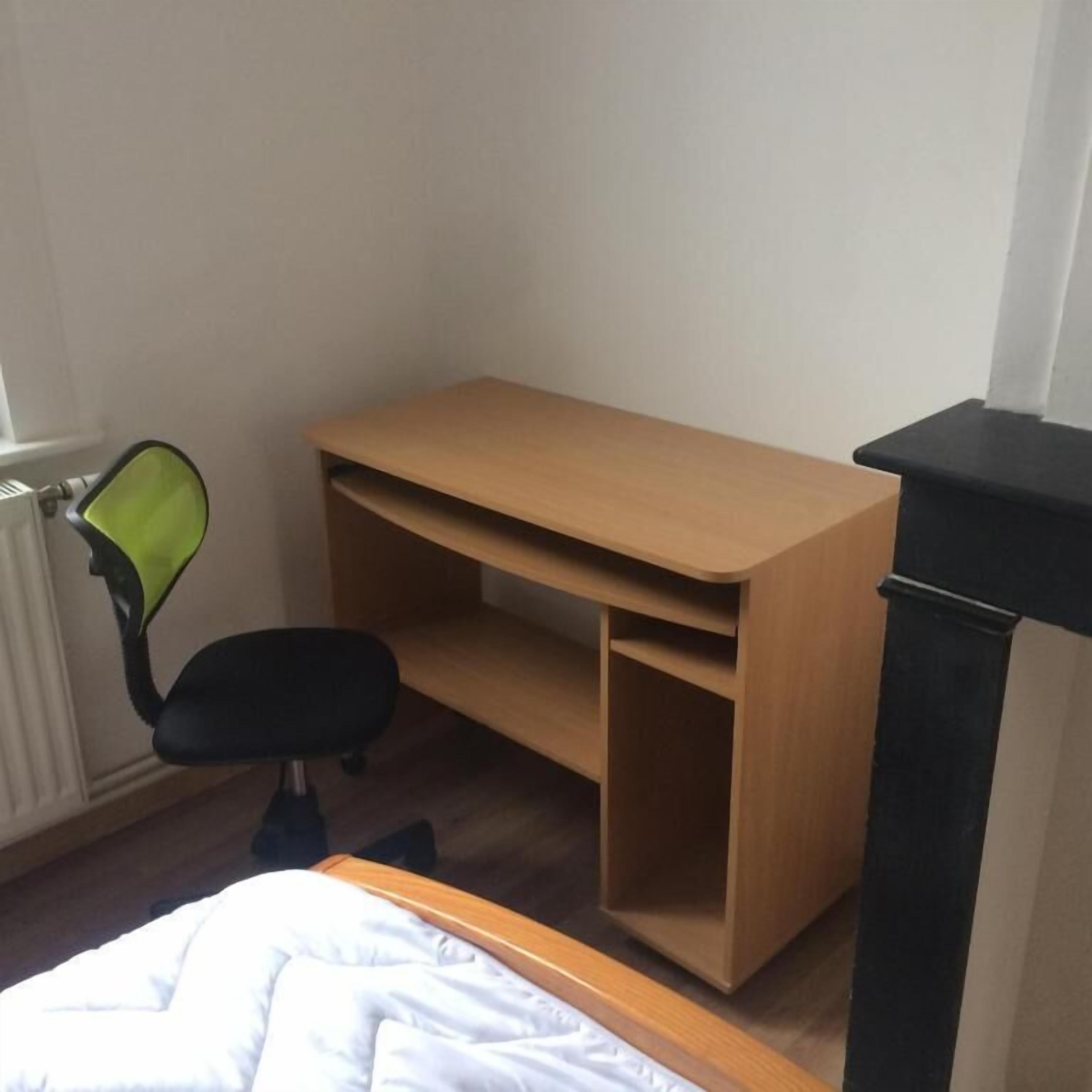Een slaapkamer met een bed, een houten bureau, een zwarte bureaustoel en een radiator.