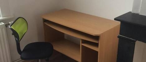 A bedroom with a bed, a wooden desk, a black office chair, and a radiator.