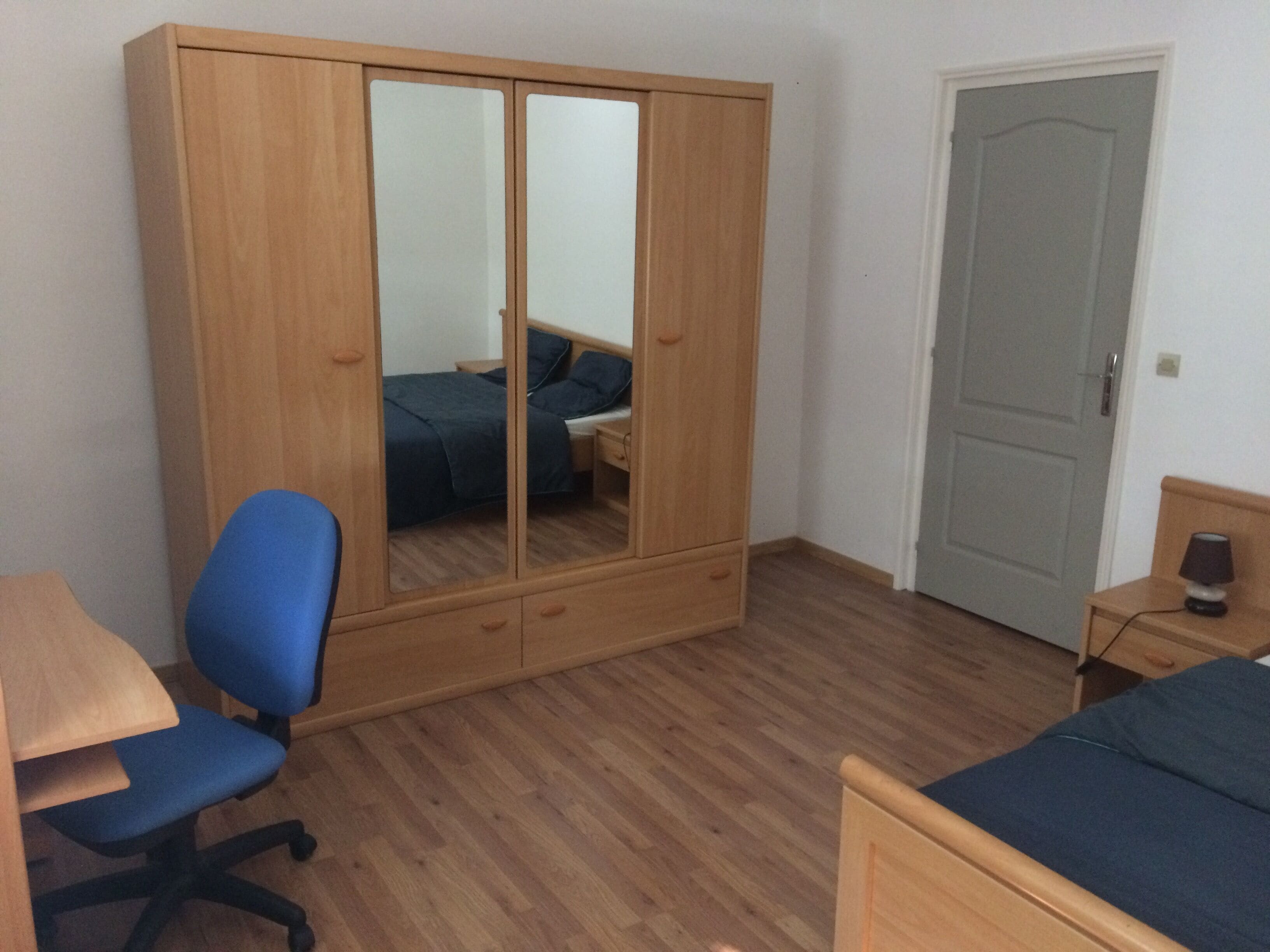Een slaapkamer met een houten garderobe, een bureau met stoel, een bed en een deur.