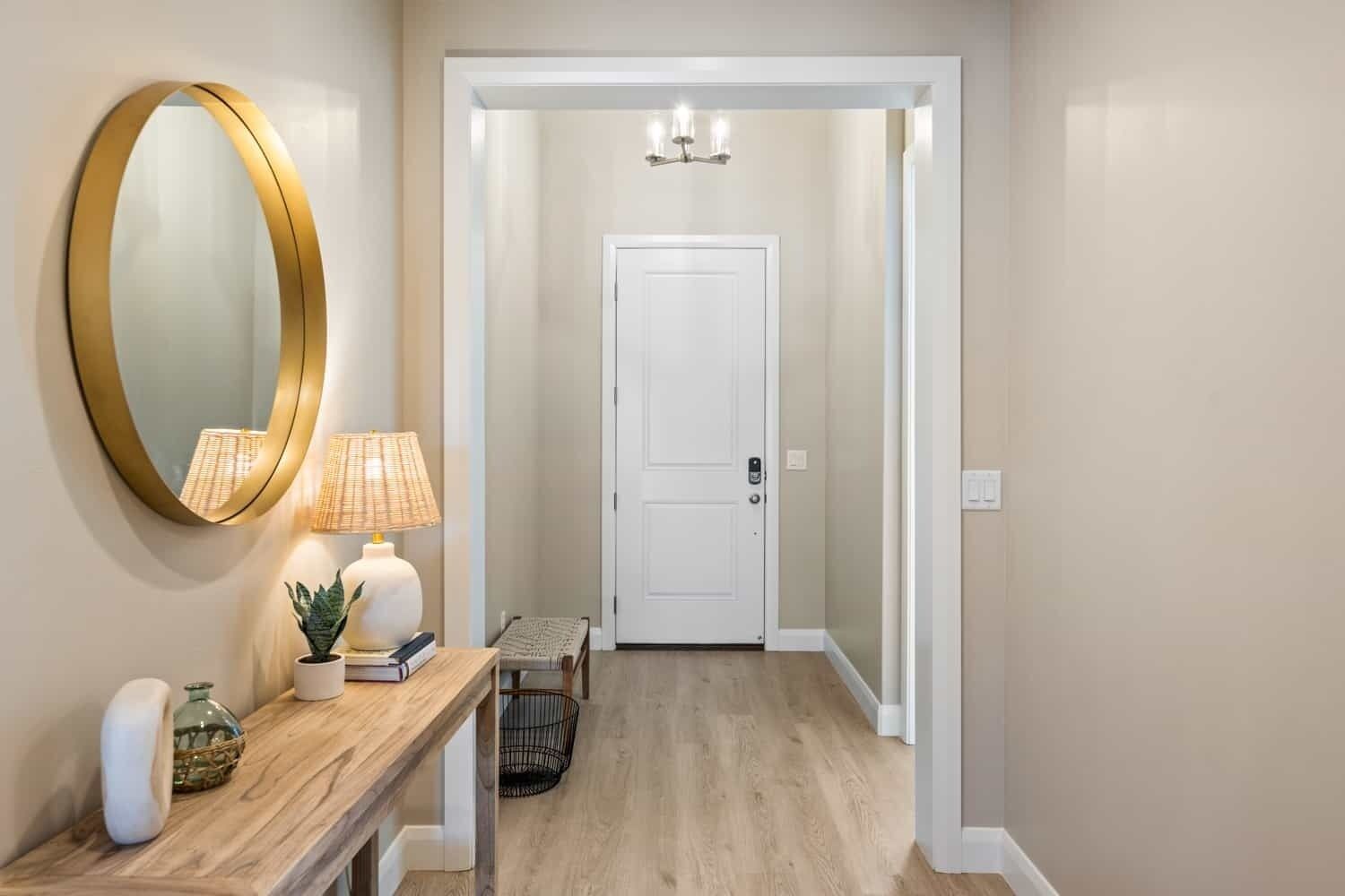 A hallway with a wooden console table, a round mirror, a door, and a small bench.