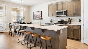 A modern kitchen with a central island, bar stools, wooden cabinets, and stainless steel appliances.