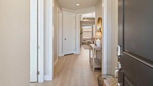 A hallway with a wooden floor, white walls, and a door with a keypad lock.