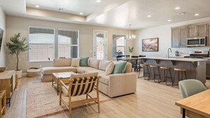 A spacious living area with a large L-shaped sofa, a dining table, and a kitchen with a central island.