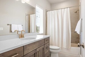 Een moderne badkamer met een witte wastafel, gouden kranen, een toilet en een douche met gordijn.
