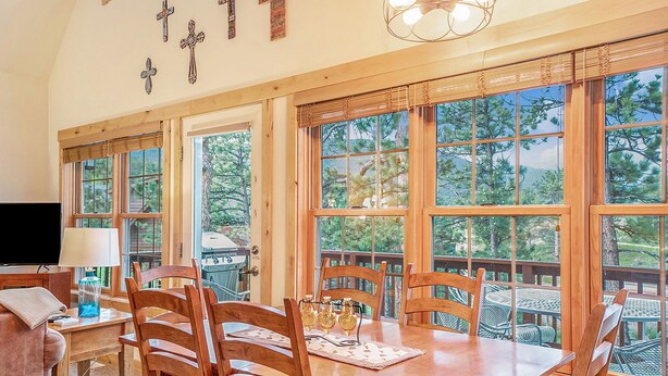 A dining area with a wooden table, chairs, and a view of trees through large windows.