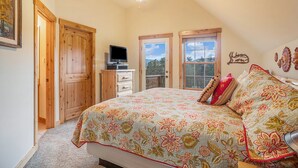 A bedroom with a large bed, a ceiling fan, a TV, and a balcony door.