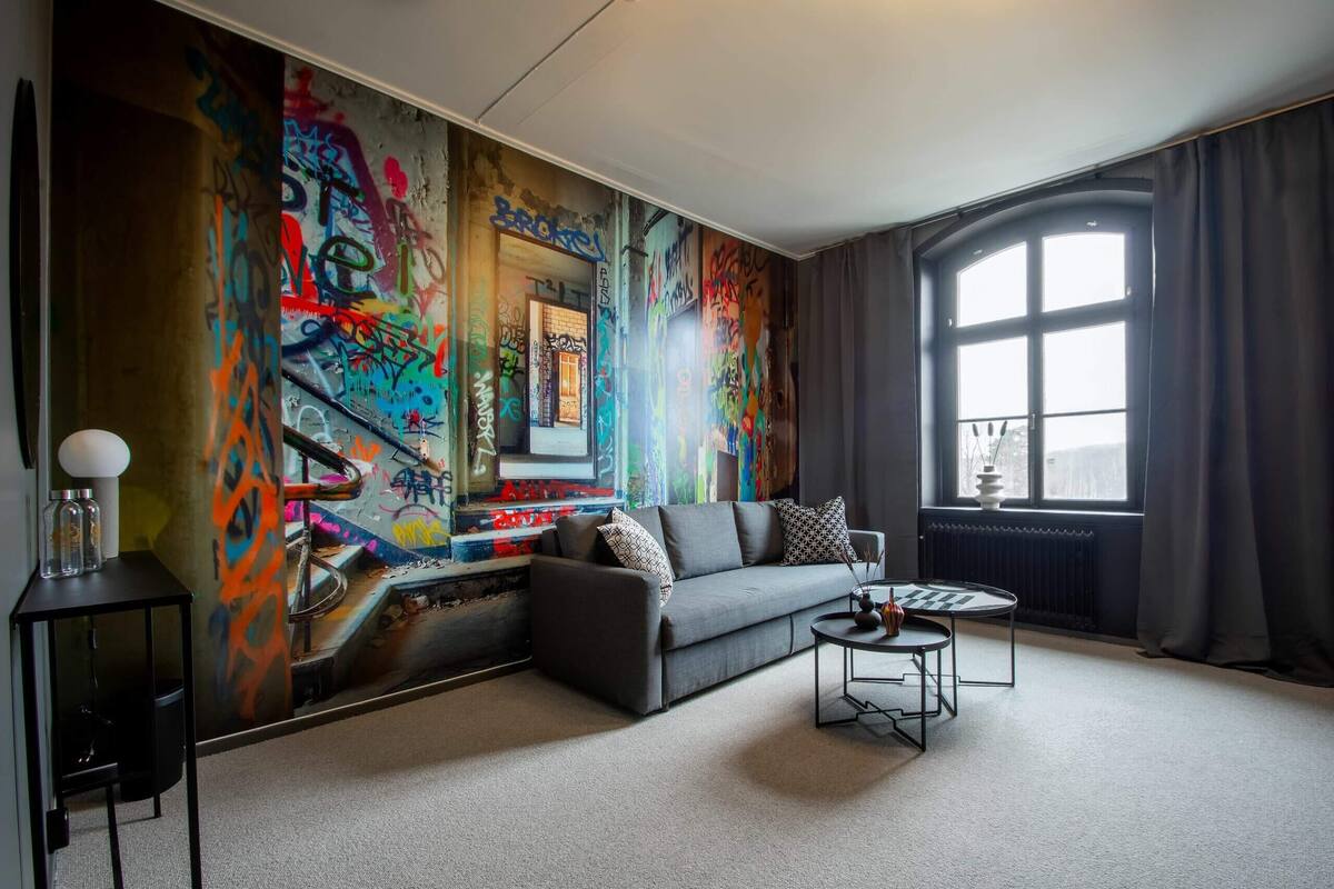 Ein modernes Wohnzimmer mit einem grauen Sofa, einem Couchtisch und einem großen Fenster mit Vorhängen.