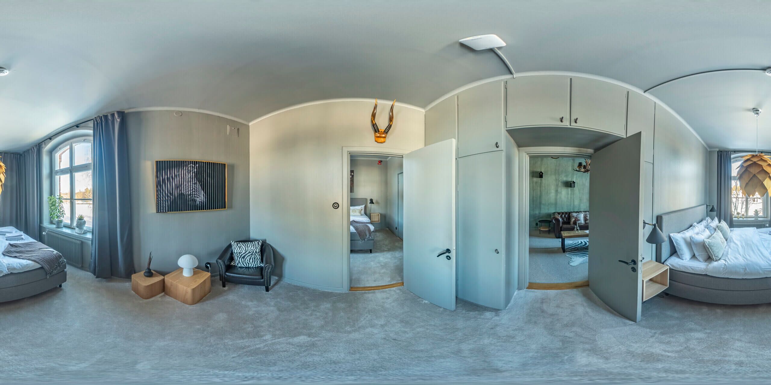 Una habitación de hotel moderna con una cama grande, una zona de estar con una silla y una mesita auxiliar, un armario y vistas de la ciudad a través de la ventana.
