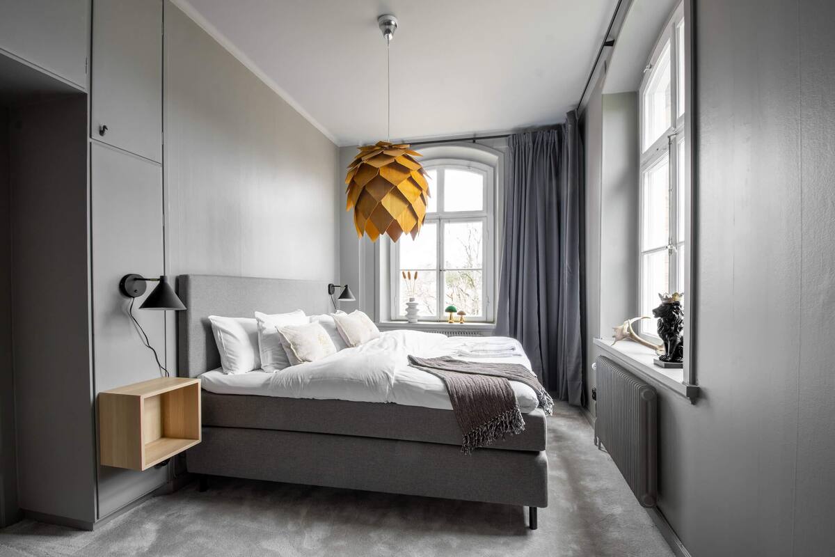 Ein modernes Schlafzimmer mit Bett, Nachttisch, Lampe und einer außergewöhnlichen Pendelleuchte.