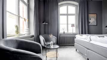 Ett modernt hotellrum med en grå soffa, ett litet runt bord, en stol och en säng.