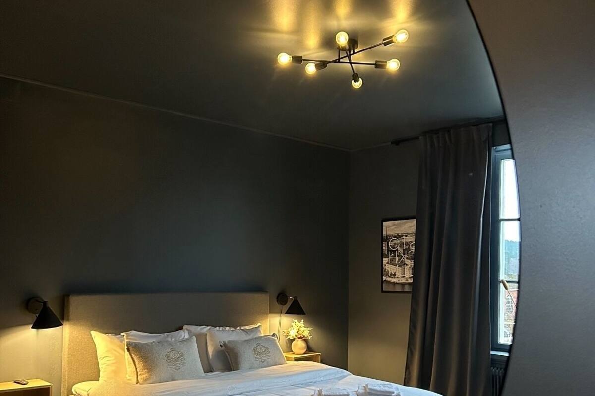 Ein modernes Schlafzimmer mit einem großen Bett, Nachttischlampen, einem Beistelltisch und Blick durch ein Fenster mit Vorhängen.