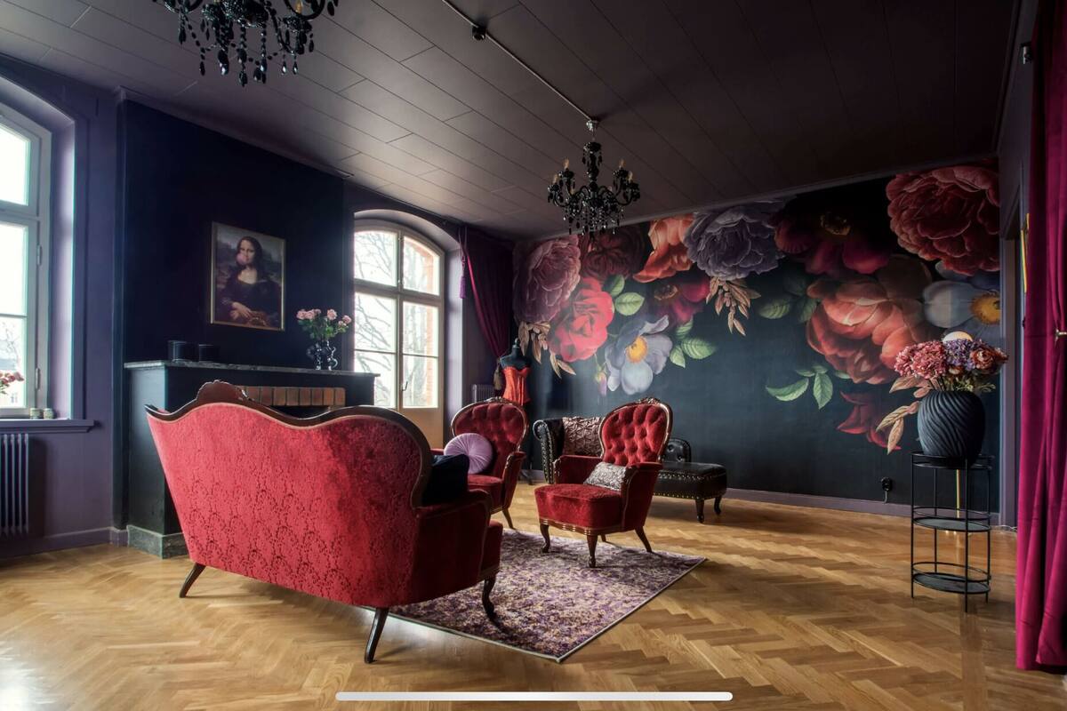 Ein Zimmer mit einer großen Blumenmalerei, einem Kamin und einem roten Sessel.