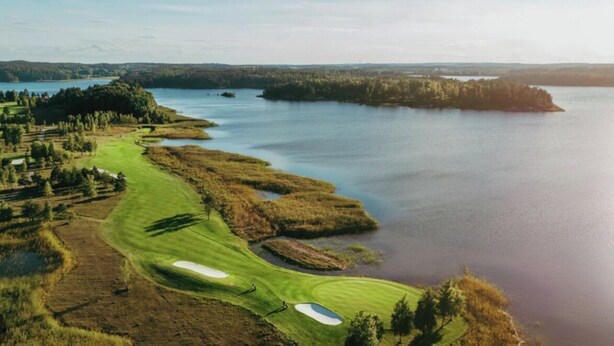 A golf course with bunkers and water hazards, surrounded by forested areas and a large body of water. - hotel montagne (Åmmeberg)