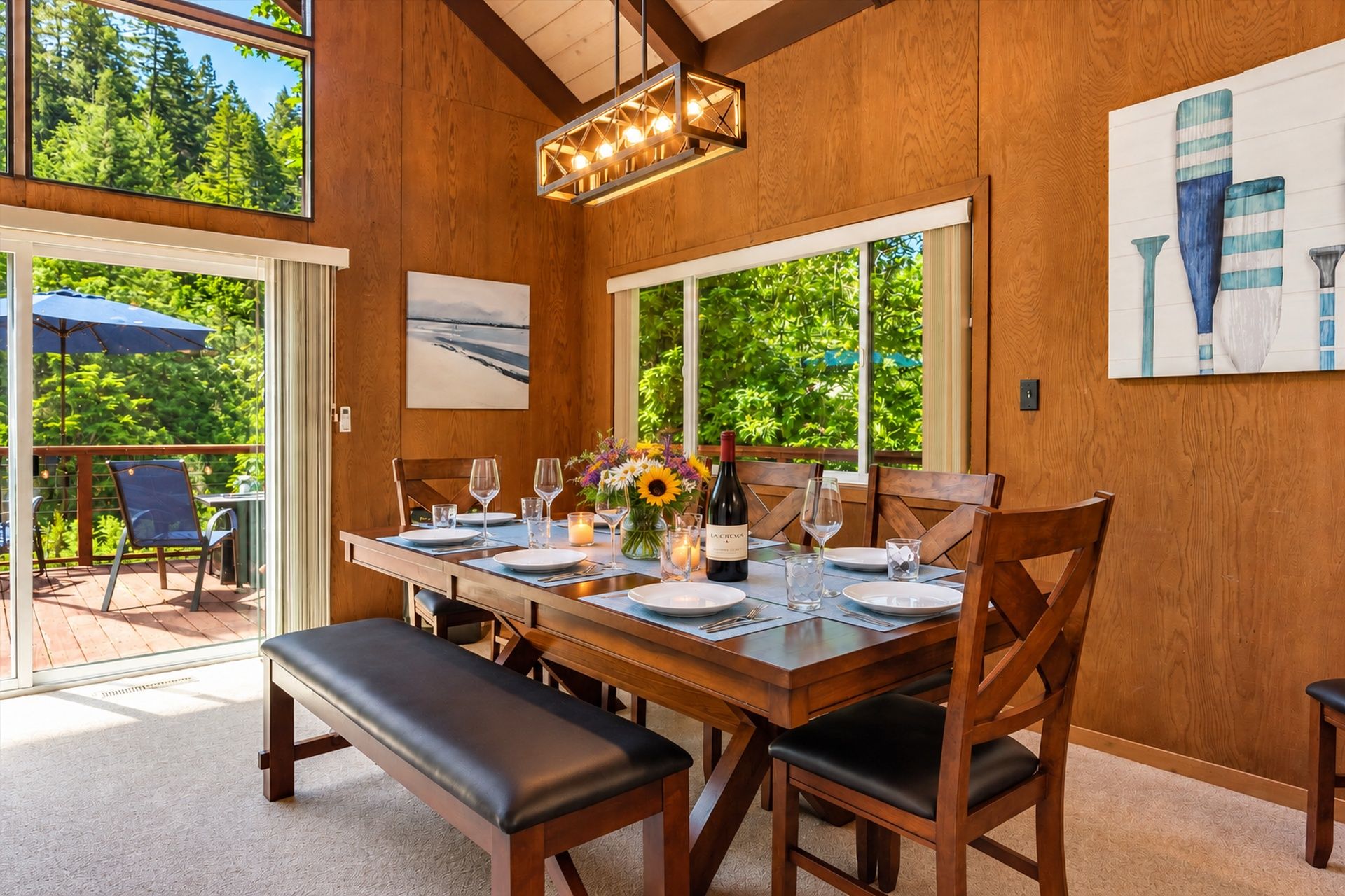 A dining area with a wooden table set for four, a bench, and a view of the outdoors.
