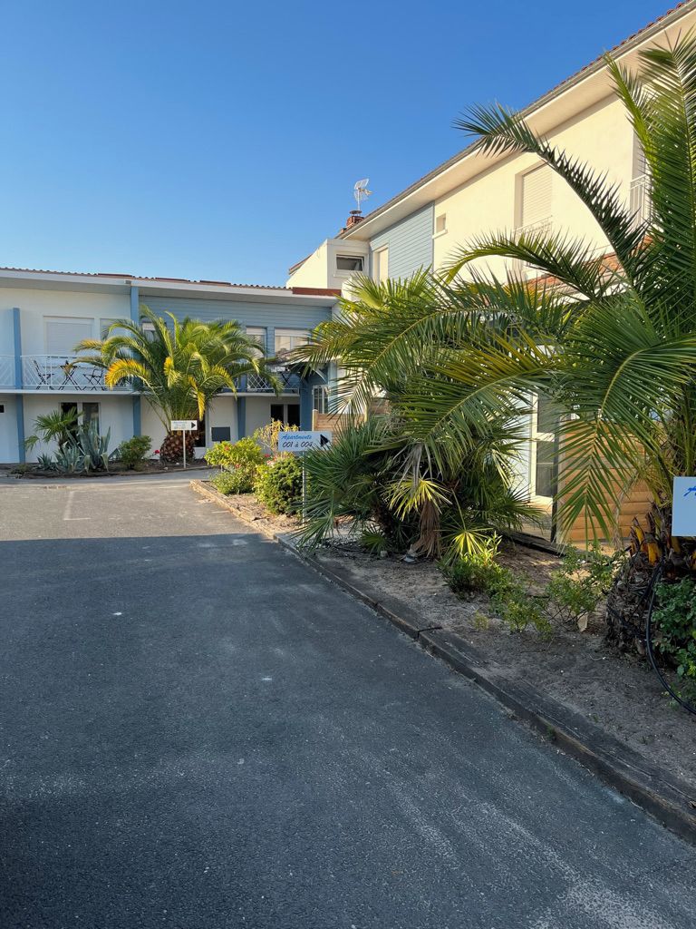 A building with multiple units, a parking area, and tropical plants.