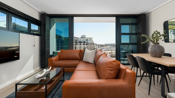 Ein modernes Wohnzimmer mit einer Ledersofa, einem Glastisch und einem Essbereich mit Holztisch und Stühlen.