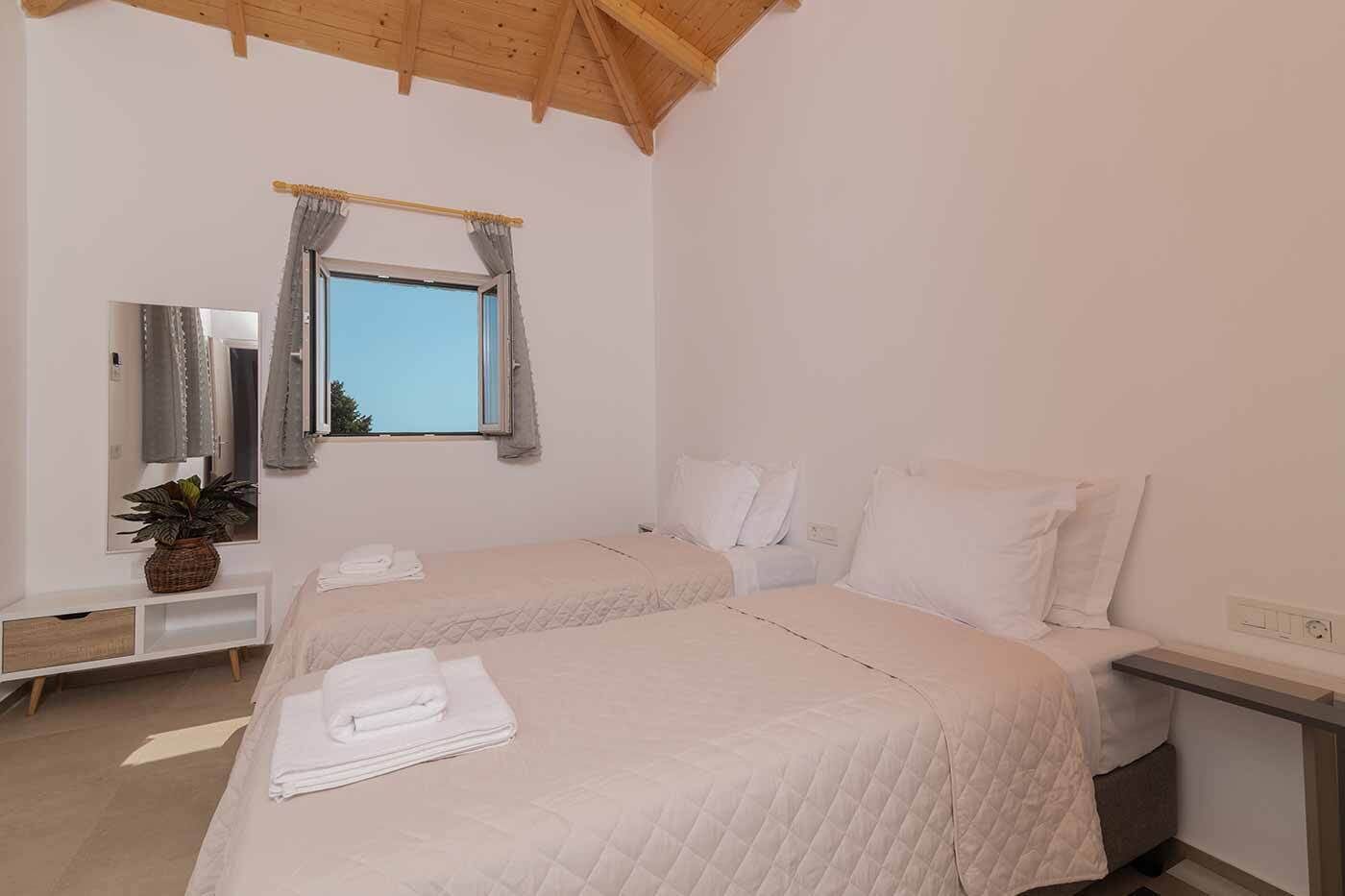 A bedroom with two beds, a bedside table, a mirror, and a window with curtains.