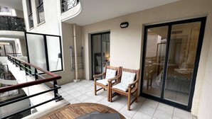 A spacious balcony with a wooden table and two chairs, a glass door leading to a dining area, and a metal railing. - Sunlight Properties MIRAGE - Nice centre with parking & terrace (Nice)