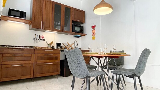 Una cuina moderna amb armaris de fusta, microones i zona de menjador amb caires i taula.