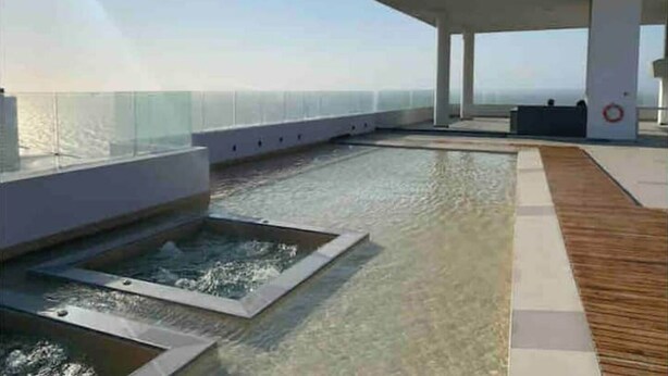 A modern rooftop deck with a pool, glass balustrade, and a wooden walkway.