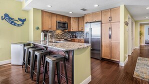 A kitchen with wooden cabinets, a stainless steel refrigerator, a microwave, and a granite countertop.