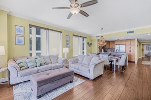 Un salon comprenant un ensemble de canapés, une table à manger avec des chaises, un coin cuisine et un ventilateur de plafond.