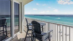 A balcony with chairs and a table overlooking a beach with people and boats.
