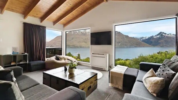 A modern living room with a large window offering a view of a lake and mountains.